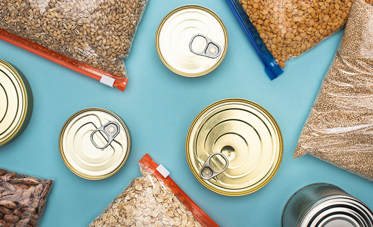 Overhead view of cans and bags with different types of cereals scattered over a light blue background.